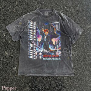May include: Dark gray t-shirt featuring a colorful graphic of a fox character in a suit, with the text "NICK WILDE" vertically on the left side. The graphic also includes the text "AGENT OF THE ZOO // SHADOW PROTOCOL".