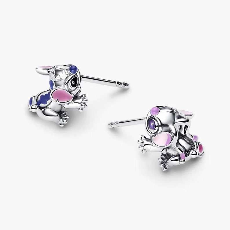 Peut inclure: Une paire de boucles d'oreilles clous argent&eacute;es repr&eacute;sentant un personnage de dessin anim&eacute;. Les boucles d'oreilles pr&eacute;sentent des d&eacute;tails en &eacute;mail bleu, rose et violet. Fond blanc.