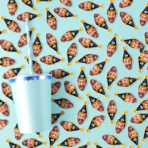 Puede incluir: Un vaso de papel azul claro con un borde azul y blanco y una pajita a rayas. El fondo es un patr&oacute;n de caras sonrientes con sombreros de fiesta negros con el n&uacute;mero "50" sobre un fondo azul claro.
