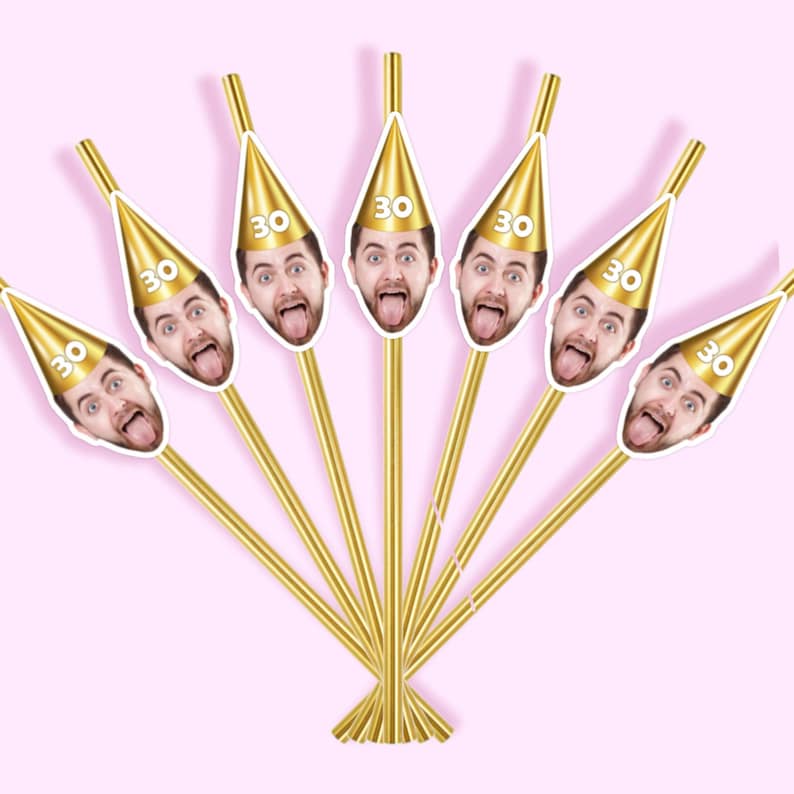 May include: A collection of six gold-colored party picks. Each pick features a photo of a person with their tongue sticking out, wearing a gold party hat with the number "30" on it. The picks are arranged in a fan shape against a pink background.