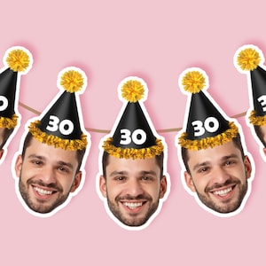 May include: A string of party decorations featuring smiling faces wearing black party hats with gold trim and yellow pom-poms. Each hat displays the number "30" in white. The background is a light pink color.