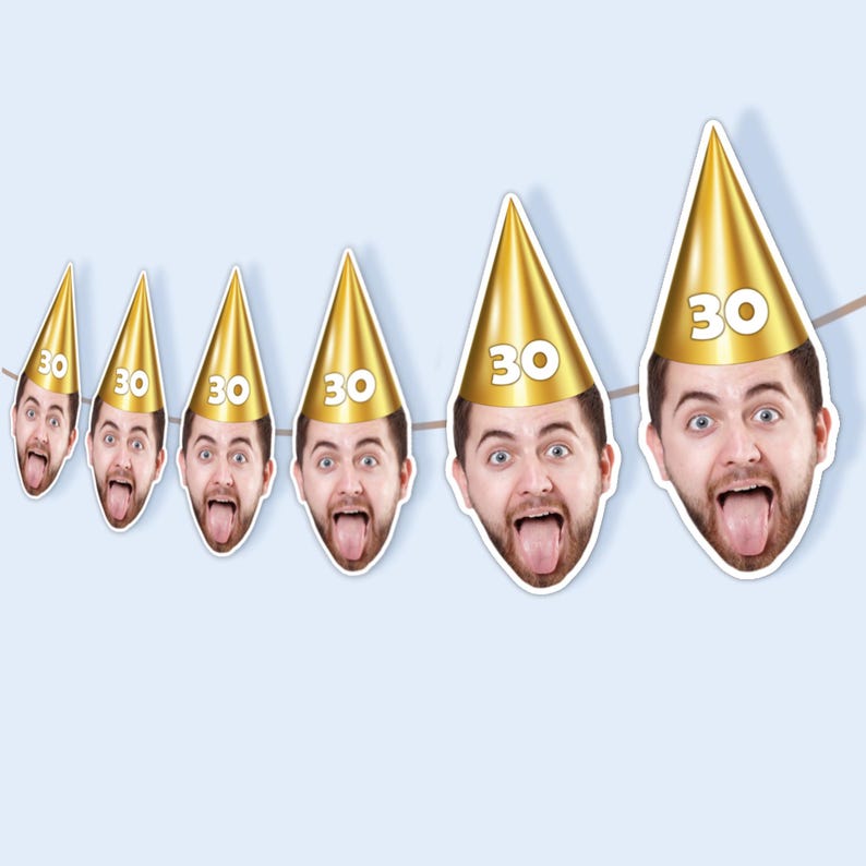 May include: A string of party decorations featuring a man's face with his tongue sticking out, wearing a gold party hat with the number 30. The decorations are strung on a brown string against a light blue background.