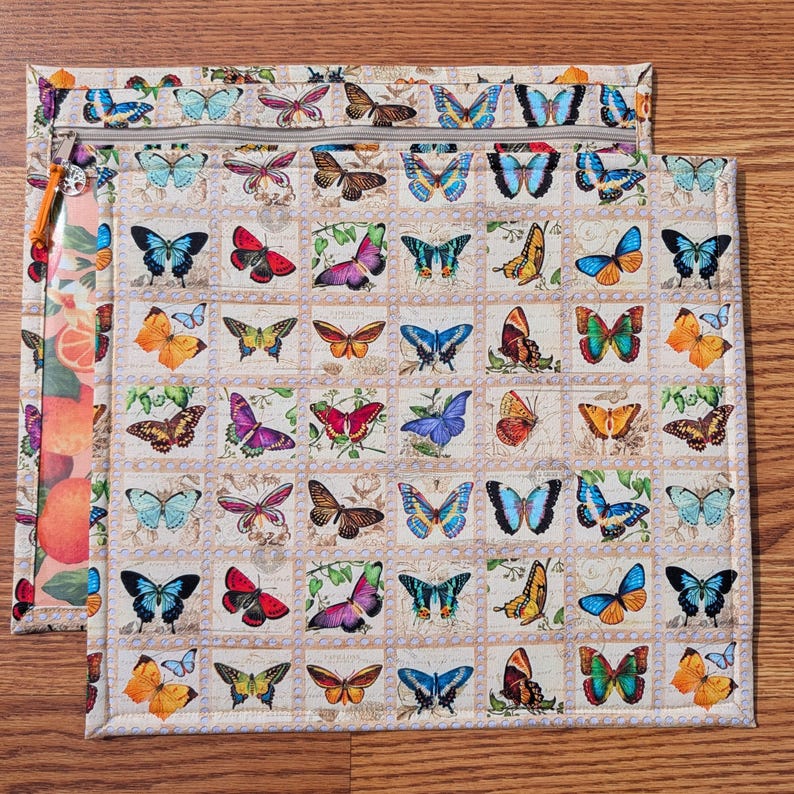 May include: Two beige quilted zipper pouches with a butterfly stamp design. The pouches feature a variety of colorful butterflies in shades of blue, red, orange, and purple. One pouch has a clear side with a fruit pattern.