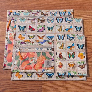 May include: A set of three zippered pouches with a butterfly and orange slice pattern. The largest pouch features a grid of colorful butterflies. The middle pouch has a clear window with orange slices. The smallest pouch has a butterfly pattern.