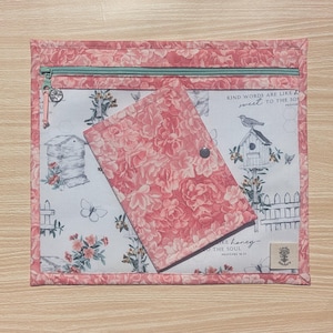 May include: A pink floral print zippered pouch with a matching small wallet. The pouch has a light green zipper and a floral pattern. The wallet has a snap closure. The background fabric has a birdhouse and bee hive design.