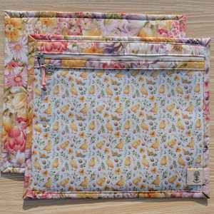 Puede incluir: Dos bolsas de tela con estampados florales y de p&aacute;jaros. La bolsa m&aacute;s grande tiene un estampado floral en tonos rosas, amarillos y morados. La bolsa m&aacute;s peque&ntilde;a tiene una cremallera y un estampado de pollitos y huevos amarillos sobre un fondo azul claro. Las bolsas son probablemente para guardar cosas.