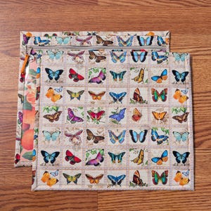 May include: Two fabric pouches with butterfly patterns. The larger pouch features a beige background with a grid of colorful butterflies. The smaller pouch has a clear plastic front with a fruit design and a beige butterfly pattern on the back. Both have zippers.