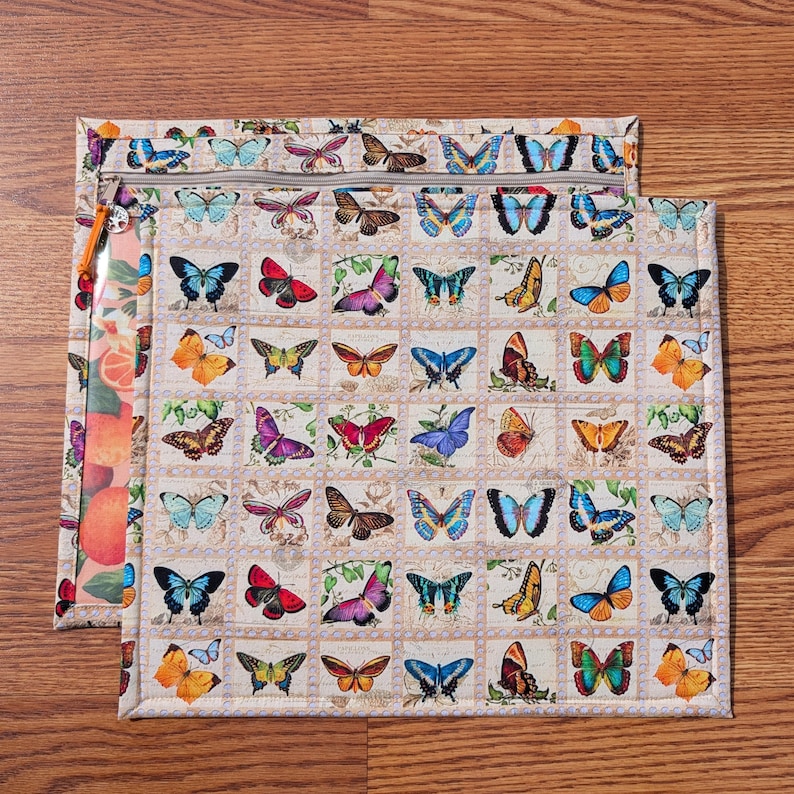 May include: Two fabric pouches with butterfly patterns. The larger pouch features a beige background with a grid of colorful butterflies. The smaller pouch has a clear plastic front with a fruit design and a beige butterfly pattern on the back. Both have zippers.