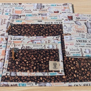 May include: Four fabric pouches with zipper closures, featuring a coffee bean pattern and text about coffee brewing methods. The text includes "Americano", "Pour Over", "French Press", and "Espresso".