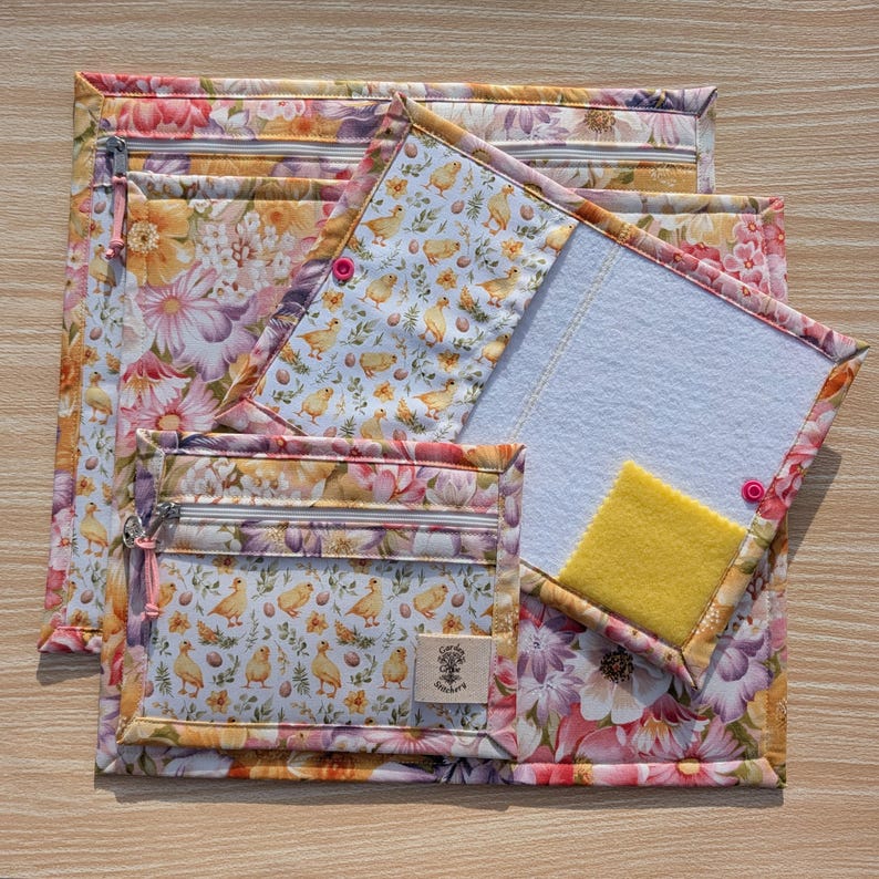 Puede incluir: Un conjunto de bolsas de tela con estampado floral y un bloc de notas. Las bolsas tienen cremalleras y un dise&ntilde;o de pollitos y huevos amarillos sobre fondo blanco. El bloc de notas tiene un interior blanco y un cuadrado amarillo.