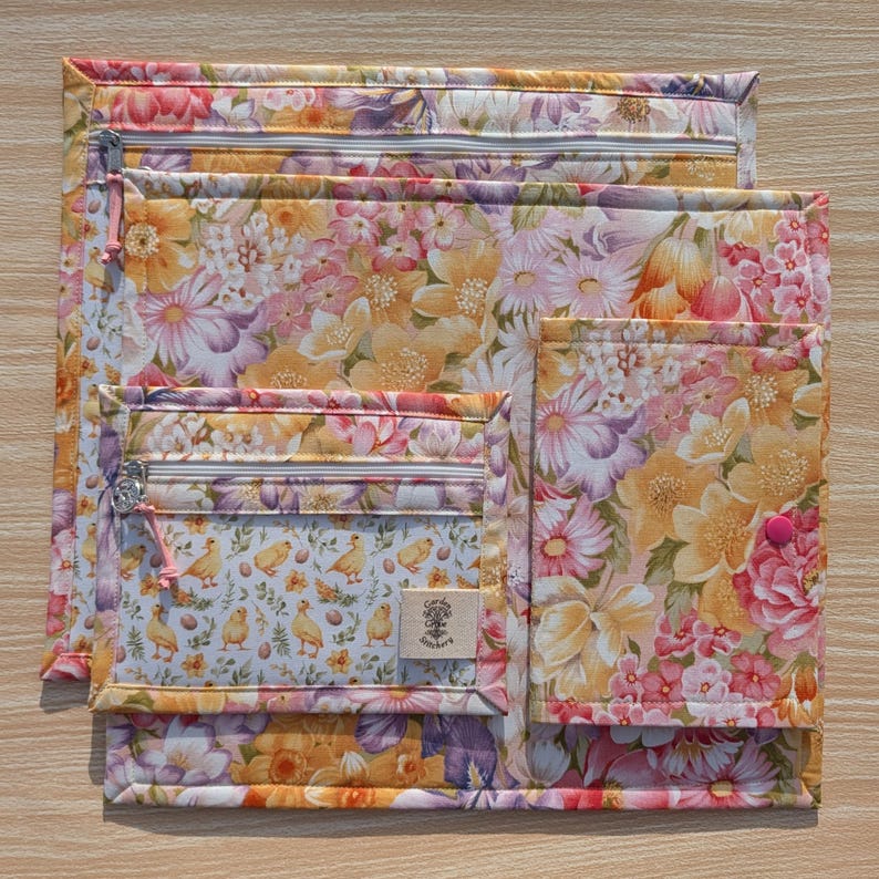 Puede incluir: Un conjunto de bolsas de tela floral de varios tama&ntilde;os. Las bolsas presentan un vibrante estampado floral en tonos de rosa, amarillo y morado. Una bolsa tiene un bolsillo m&aacute;s peque&ntilde;o con un estampado de pollitos y huevos. Cada bolsa tiene cierre de cremallera.