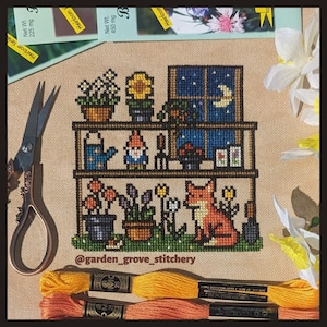 May include: Cross-stitch embroidery of a whimsical garden scene with a fox, a gnome, and a shelf of potted plants. The scene is set at night with a window showing a crescent moon and stars. The embroidery is signed "@garden_grove_stitchery".