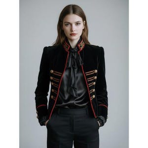 May include: A black velvet jacket with gold buttons and red trim. The jacket features a high, embroidered collar and is worn with a black satin blouse and trousers. The design of the jacket is similar to a military style.