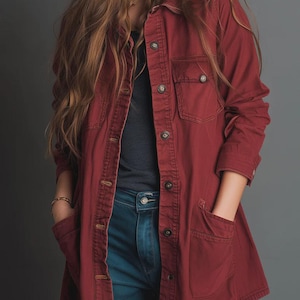 May include: A long-sleeved, burgundy shirt-jacket with two chest pockets and two lower pockets. The shirt has a button-up front and is paired with blue jeans. The model is wearing a gold bracelet.