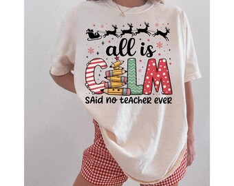 Könnte beinhalten: Cremefarbenes T-Shirt mit dem Aufdruck "all is calm said no teacher ever". Das Design zeigt einen Rentierschlitten, Schneeflocken und das Wort "calm" mit einem Bleistiftstapel und Tupfen.