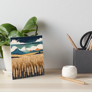 Puede incluir: Una impresión artística rectangular que representa un campo de trigo bajo un cielo azul con nubes blancas y montañas. El campo de trigo está en primer plano, con las montañas al fondo. La paleta de colores incluye tonos de azul, amarillo y marrón.
