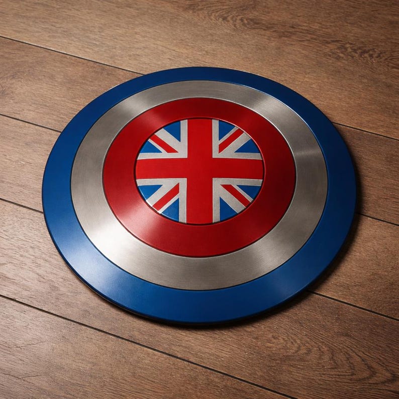 May include: A circular shield with a blue border, a silver central band, and a red center displaying the Union Jack. The shield is made of metal and is likely a decorative item or collectible.