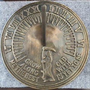 May include: A bronze-colored sundial with Roman numerals and a central gnomon. The sundial features the text "Grow along the best" and "Old with is yet to be" and a depiction of the Grim Reaper.
