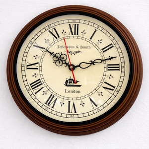 May include: Round wall clock with a dark brown wooden frame. The clock face is cream-colored with black Roman numerals and hands. The clock reads "Jeffereann & Smith" and "London". The second hand is red.