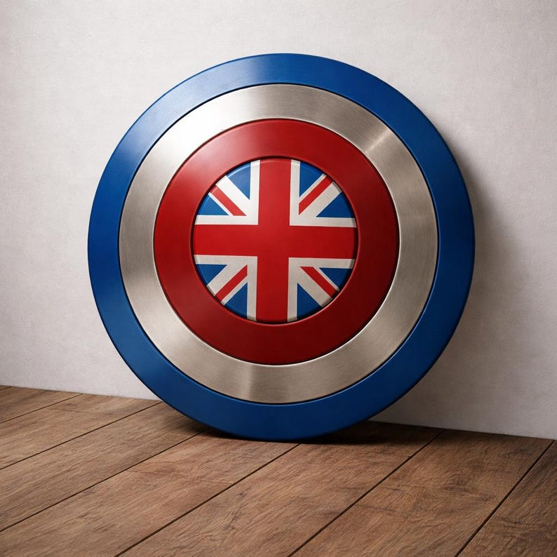 May include: A circular shield featuring the Union Jack flag at its centre, surrounded by a red ring, a silver ring, and a blue outer ring. The shield is displayed against a white wall and wooden floor.