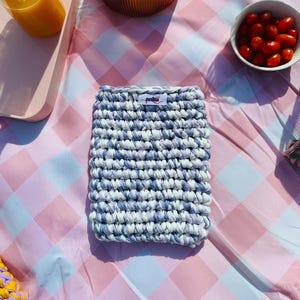 Könnte beinhalten: Handgefertigte, rechteckige Häkeltasche in Blau- und Weißtönen mit einem kleinen Etikett "anita". Sie liegt auf einer rosa-weiß karierten Picknickdecke, zusammen mit Tomaten, Äpfeln und einem Glas Saft.