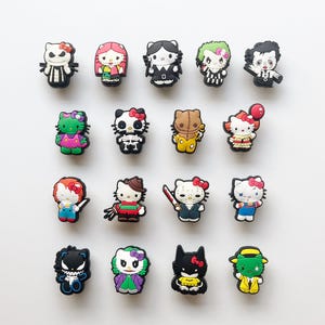 Może przedstawiać: Kolekcja szesnastu kolorowych gumowych przypinek do butów z różnymi wzorami postaci, w tym Hello Kitty przebraną za kultowe postacie z horrorów i popkultury, takie jak szkielet, klaun, superbohater i zamaskowany morderca, ułożonych w cztery rzędy.