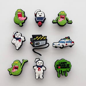 May include: Nine colorful shoe charms featuring characters and elements from the Ghostbusters franchise. Includes the Stay Puft Marshmallow Man, Slimer, a proton pack, and the Ecto-1 car. The phrase "I AIN'T AFRAID OF NO GHOSTS" is also featured.