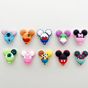 May include: Ten colourful cartoon mouse-shaped charms are displayed. Each charm has a unique design, with colours including blue, orange, red, pink, green, and black. The charms are likely for decorative purposes.