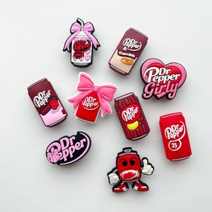 May include: A collection of colorful Dr. Pepper-themed charms. The charms include soda cans, bows, and heart shapes, with text such as "Dr Pepper Girly" and "Diet". The charms are in shades of red, pink, and brown.