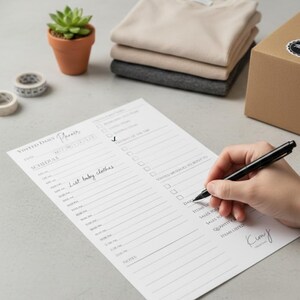 May include: A person's hand writing on a white Vinted Daily Planner with a black pen. The planner includes a schedule and checklist. A small potted succulent, rolls of tape, and folded clothing are in the background.