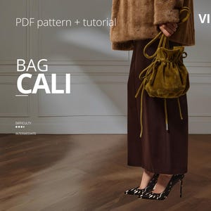 Puede incluir: Una persona sostiene un bolso con cordón de color verde oliva con cordones largos y finos. El texto "BAG CALI" se muestra en blanco, junto con "PDF pattern + tutorial" y "VIKISEWS". La dificultad se indica como intermedia.