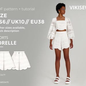 May include: A woman models a white, eyelet crop top and shorts set. The shorts have a scalloped hem. The image includes text indicating the pattern is a PDF tutorial for "SHORTS SORELLE" in sizes US6, UK10, and EU38. The difficulty level is intermediate.