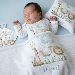 Pode incluir: Um bebé a dormir sob um cobertor branco com uma estampa de girafa, elefante e leão. O bebé usa um body branco com desenhos de animais e luas a condizer. Uma almofada e um babete com o mesmo desenho também são visíveis.