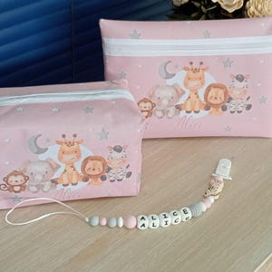 Pode incluir: Duas bolsas de cosméticos rosa com uma estampa de animais de desenho animado, incluindo um macaco, um elefante, uma girafa, um leão e uma zebra. As bolsas têm um zíper branco e o nome "Alice" impresso nelas. Também há um prendedor de chupeta com o nome "ALICE".