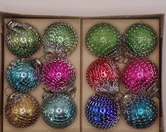May include: A set of twelve spherical ornaments arranged in a cardboard box. Each ornament features a vibrant, reflective glass surface in shades of green, blue, pink, red, and gold, encased in a decorative silver-toned wire mesh netting.