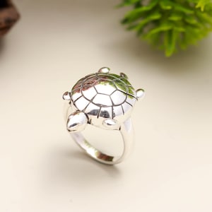 May include: A silver ring with a turtle design. The turtle's shell is detailed, and the ring has a polished finish. The ring is a piece of jewellery.