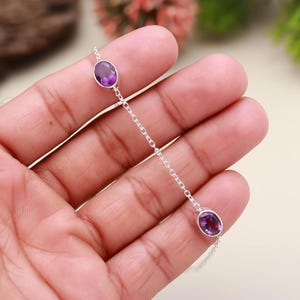 Peut inclure: Un bracelet en chaîne argentée orné de trois pierres d'améthyste ovales, d'un violet profond. Les pierres sont espacées le long de la chaîne, créant un design minimaliste. Le bracelet est présenté sur un fond neutre et doux.
