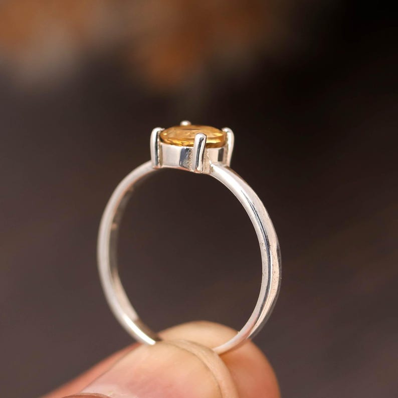 Puede incluir: Un anillo de plata con una sola piedra preciosa amarilla, redonda y facetada, montada en un engaste de cuatro garras. La banda es fina y pulida, mostrando un acabado met&aacute;lico liso. La piedra preciosa se sit&uacute;a en la parte superior del anillo.