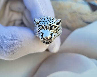May include: A silver ring with a leopard head design. The ring depicts the leopard's face, with detailed eyes, nose, and spots. The ring has a polished finish and is a striking piece of jewellery.