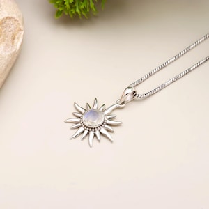 May include: A silver pendant necklace with a sunburst design. The pendant features a central, round, iridescent stone, encircled by pointed rays. The chain is a delicate, textured silver.