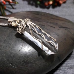 以下が含まれることがあります： シルバーカラーの金属製のセッティングとチェーンが付いた、透明な水晶ペンダント。クリスタルはファセットカットされており、先端が尖っています。金属製のセッティングは上部に装飾的なデザインが施されています。