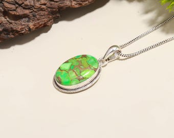 Puede incluir: Un collar con colgante de plata con una piedra ovalada verde y marrón. La piedra está engastada en un bisel de plata con un borde en forma de cuerda. La cadena del collar también es de plata y tiene un diseño delicado y enlazado.