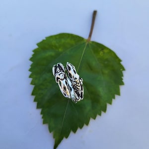 Peut inclure: Une bague argentée au design orné, avec des détails ajourés et texturés. La bague est présentée sur une feuille verte sur fond blanc, mettant en valeur son savoir-faire complexe et son style unique.