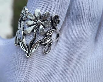 May include: A silver-toned ring featuring a daisy flower design with detailed petals and leaves. The ring has an openwork design with a floral theme, perfect for adding a touch of nature-inspired elegance to any outfit.
