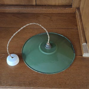 Peut inclure: Une suspension vintage verte avec une rosace de plafond en céramique blanche et un cordon torsadé en tissu. Le luminaire a un abat-jour circulaire émaillé. Le cordon est beige et l'abat-jour est vert.
