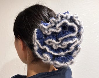 May include: A large, handmade scrunchie in a flower shape. The scrunchie features a layered design with alternating bands of navy blue, grey, and white yarn. The accessory is worn in the hair, adding a unique touch to any hairstyle.