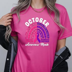 A person wearing a pink t-shirt with a graphic design related to breast cancer awareness, including a rainbow and text.
