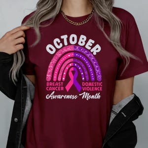 A person wearing a maroon t-shirt with a graphic design related to breast cancer awareness, including a rainbow symbol and text.