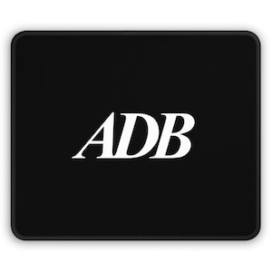 Puede incluir: Alfombrilla de ratón rectangular negra con esquinas redondeadas. La alfombrilla presenta las letras mayúsculas blancas "ADB" en una fuente serif, centradas en la almohadilla.