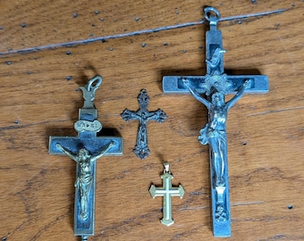 Op de afbeelding: Een verzameling van vijf kruisbeelden van verschillende groottes en ontwerpen. De kruisbeelden zijn gemaakt van metaal en tonen gedetailleerde afbeeldingen van Jezus Christus. De kruisen zijn in zilver, goud en brons, sommige vertonen tekenen van ouderdom en slijtage.
